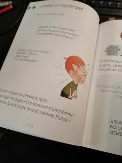 Un livre ouvert avec une illustration d'un enfant en colère, posé sur une table. Le texte est en français et pose des questions sur les désirs et les règles.